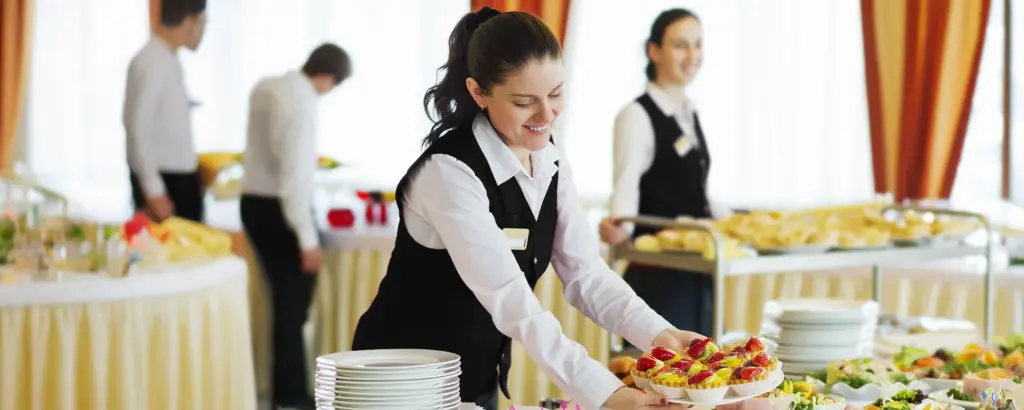 Kellnerin im Service, trägt Tablett mit Desserts in einem eleganten Buffet-Raum. Empfang oder Veranstaltung.