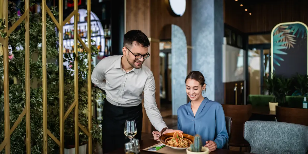 Ein Kellner serviert einer Frau in einem schicken Restaurant ein stilvolles Gericht mit einem Lächeln.